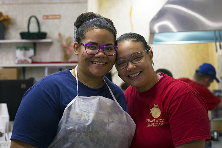 Pankiewicz Cider Mill & Farm Market employees and sisters, Charlene Hardy and Alyssa Hardy, pose for a photo in between prepping donuts.
