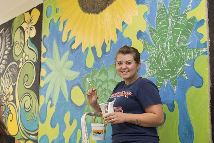 Artist and Goodells resident, Dakoda Shaw poses with the mural she created with support from her mother, Denise Jones. 

"A lot of people know that I love art and somebody recommended it [the project] to me at work," says Shaw. "I picked these succulents here because down at the end of Desmond's Landing every weekend they have a farmers market and I actually bought succulents on there and they are lavishing. This is to kind of help grow the community, so why not grow with the succulents?"