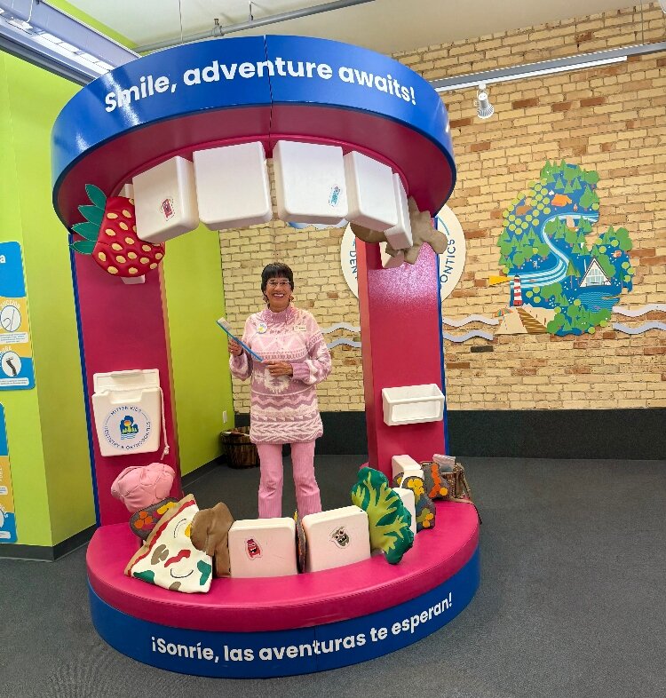 Dr. Jessica Rickert, DDS, stands inside the GRCM’s oversized mouth exhibit, holding an oversized toothbrush.